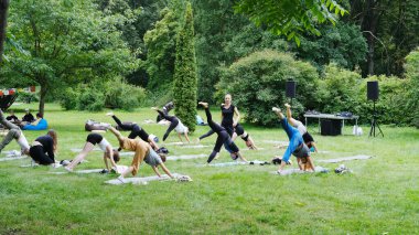 Minsk, Belarus - 06 Mayıs 2025: Canlı bir park ortamında grup yoga oturumu, çeşitli katılımcıların yeşilliklerle çevrili paspaslar üzerinde poz vermeleri