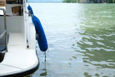 Durgun sularda mavi çamurluğu olan, yemyeşil tepeleri olan ve arka planda berrak gökyüzü olan bir teknenin yan görüntüsü.