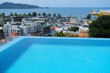 Sonsuz havuz kenarı, parlak bir gökyüzünün altındaki yeşil tepelerle çevrili modern mimari ve okyanus dalgalarıyla muhteşem bir kıyı kenti manzarası sağlar.