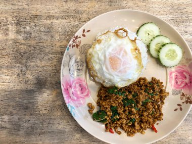 Kızarmış pilav, kıymalı ve yumurtalı otlarla kaplı, salatalık dilimleri ile ahşap bir masada servis edilen dekoratif tabakta.