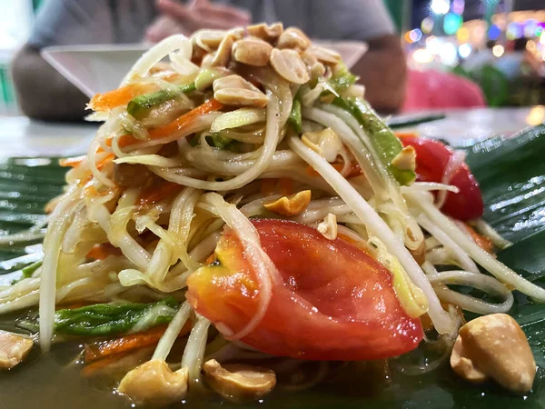 Muz yaprağında servis edilen doğranmış sebze, fıstık ve domateslerden oluşan Pad Thai salatası. Arka planda bulanık bir yemek alanı var.