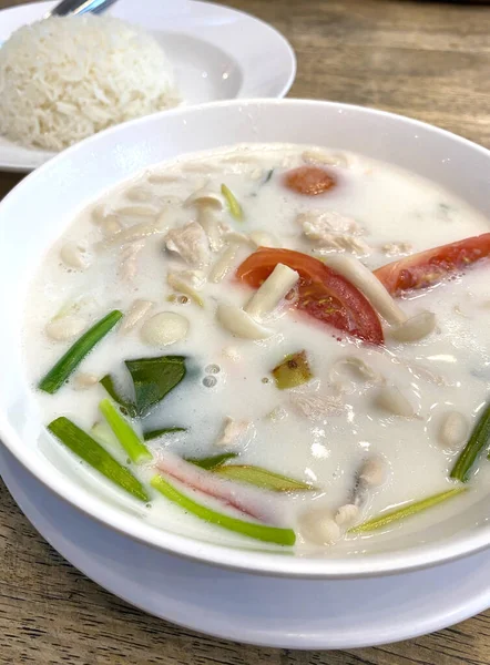 Tavuklu, domatesli ve otlu kremalı hindistan cevizi çorbası ahşap bir masada, yanında pilav ile servis edilir.