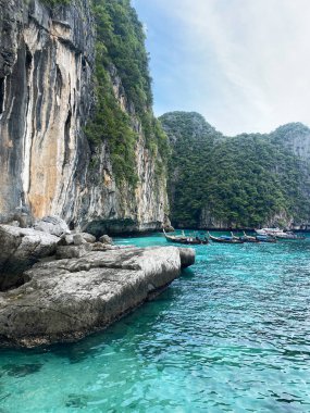Tayland 'daki turkuaz suların üzerinde yükselen kireçtaşı kayalıkları, bölgeyi çevreleyen yemyeşil yemyeşil bir kıyı şeridinin yakınındaki geleneksel uzun kuyruklu teknelerle dolu.