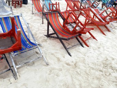 Çizgili desenli renkli ahşap plaj sandalyeleri arka planda daha fazla sandalye ve plaja gidenlerle çevrili kumlu plaja yerleştiriliyor.