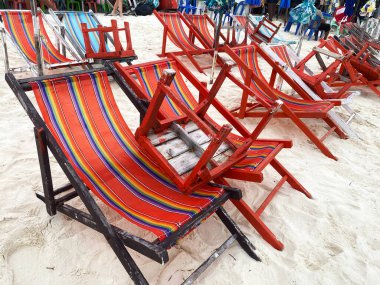 Kumlu bir sahilde renkli çizgili istiflenmiş plaj sandalyeleri, arka planda daha fazla sandalye, kıyı rahatlama ortamı için ideal.