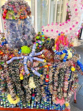 Geri dönüştürülmüş plastik eşyalardan yaratılan renkli dekoratif düzenleme, çeşitli şekil ve dokuların sergilenmesi, şehir ortamında bir el arabasında sergileniyor.