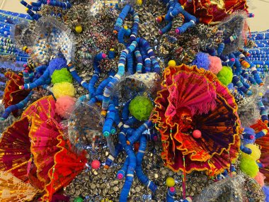 Geri dönüşüm ve yaratıcılığı vurgulayan canlı bir kurulumda düzenlenmiş kurdele, boncuk ve ponpon gibi kullanılmış plastik eşyaların sanatsal gösterimi