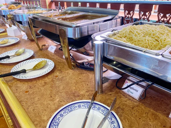 Tayland büfesi, içinde erişte ve soslar bulunan metal tepsiler ve ahşap bir masa. Konukların keyfine varmaları için tabaklar ve servis aletleri de var.