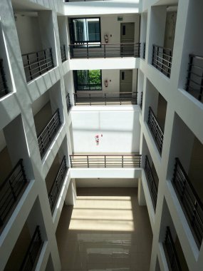 Modern çok katlı bir binanın iç manzarası, açık bir avlu, içeri doğal ışık akışı ve her katta parmaklıklar olan balkonlar.