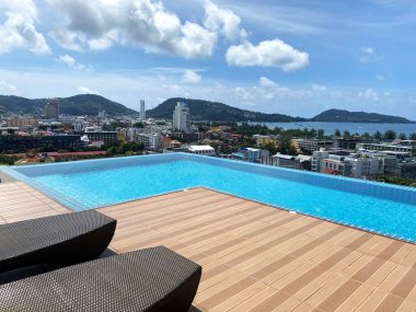 Ahşap güverteli ve şezlonglu sonsuz çatı havuzu, parlak mavi gökyüzünün altında şehrin ve dağların panoramik manzarasını sunuyor.