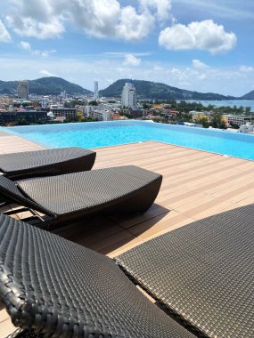 Ahşap bir güvertede şezlonglar bulunan sonsuz çatı havuzu, berrak mavi gökyüzünün altında şehrin ve dağların panoramik manzarasını sunuyor.