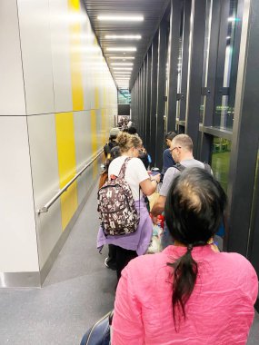 İstanbul, Türkiye - 20 Ekim 2025: Yolcular cam duvarlı ve parlak sarı aksanlı çağdaş bir havaalanı terminalinde uçağa binmek için sıraya giriyorlar