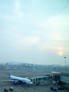Mumbai, Hindistan - 21 Ekim 2025: Mumbai Uluslararası Havalimanı 'ndaki Indigo Havayolları uçağı günbatımında arka planda terminal kapısı ve şehir silüeti ile