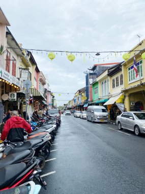 Phuket, Tayland - 28 Ekim 2025: Phuket Old Town 'da renkli mimari, ıslak bir cadde boyunca park etmiş, üzerinde dekoratif fenerler bulunan motosikletlere ev sahipliği yapıyor.