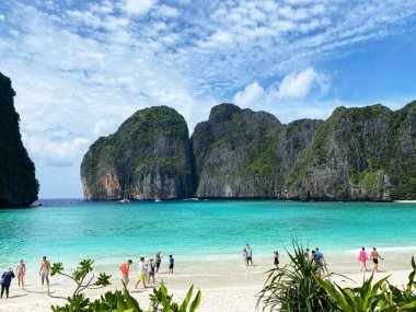 Maya Körfezi Adası, Tayland - 30 Ekim 2025: Maya Körfezi Adası turkuvaz suları ve kireçtaşı kayalıkları ile turistlerin yemyeşil kumsalda yürüdüğü