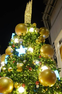 Altın süsler ve parlak ışıklarla süslenmiş Noel ağacı, tepesinde bir yıldız, ışıl ışıl bir gece ortamında neşeli bir neşe saçıyor.