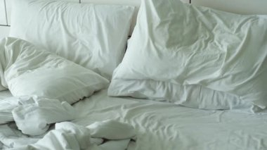 Kırışık beyaz çarşafları ve dağınık yastıkları olan dağınık bir yatak odası, yukarıdan bakıldığında rahat bir atmosfer yaratıyor.