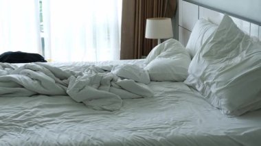 Kırışık beyaz çarşaflar ve yastıklarla döşenmemiş, perdelerin doğal ışığıyla aydınlatılmış, yatak odasındaki rahat atmosferi geliştiren,