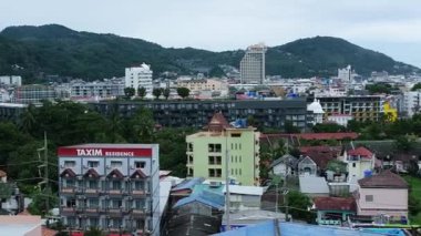 Phuket, Tayland - 22 Ekim 2025: Phuket şehrinin kentsel yapıları, yemyeşil bitki örtüsünü ve arka planda görünen bir yolcu gemisiyle kıyı şeridini vurgulayan hava perspektifi