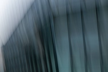 Modern mimari bir binanın dış cephesinin soyut dikey hareket bulanıklığı. Bu kasıtlı kamera hareketi (ICM), çağdaş kentsel yapının mavi ve metalik tonlarını vurgulayarak, ışık ve gölgenin ritmik ve resmî bir efektini yaratır..