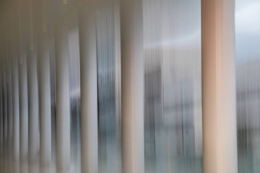 Modern bir binanın ön cephesinin dikey çizgilerinin olduğu çağdaş bir soyut görüntü. Cam, çelik ve ışığı resmedilmiş, minimalist bir kompozisyonda harmanlamak için kasıtlı Kamera Hareketi (ICM) teknikleri kullanılmıştır..