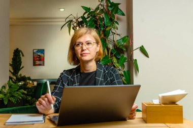 Gözlüklü kadın dizüstü bilgisayarında rahat bir kafe ortamının keyfini çıkarıyor..