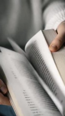 Bir kız hızla kucağında uzanan bir kitabın sayfalarını çevirir. Yakın plan. Dikey video.