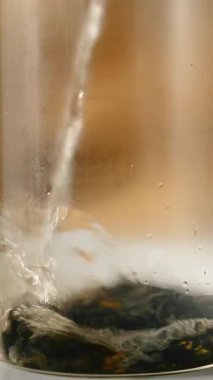 Sıcak su yavaşça berrak bir bardak çaya dökülür. Yakın plan. Dikey video.