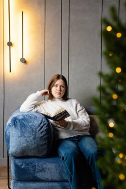 Evdeki mavi koltukta oturan kadın kitap okuyor, rahat iç mekan, rahat yaşam tarzı ve hafif ışıklandırma..
