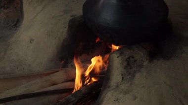 Kırsal bir mutfak ortamında yanan odun ateşiyle beslenen geleneksel bir kil soba. Geleneksel yemek pişirme yöntemlerini, kırsal yaşam tarzını ve kültür mirasını temsil eden toprak ocağı yapısı ve parlayan ateşin yakın görüntüsü.