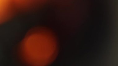 Yumuşak turuncu bokeh ışığı ve pürüzsüz hareket bulanıklığı içeren koyu soyut bir arka plan. Odaklanamayan parıltı sinematik ve karamsar bir atmosfer yaratıyor, örtüşmeler, geçişler, başlık arkaplanları, sanatsal görseller ve modern video tasarım projeleri için ideal..