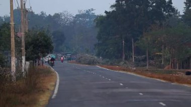 Dibrugarh, Assam, Hindistan, 10 Ocak 2026: Assam 'da yayalar ağaçlar, elektrik direkleriyle çevrili ve Assam' daki köy evleriyle çevrili bir yolda yürürken, motosikletliler kaldırımlı bir yolda ilerliyorlar. Olay yeri günlük ulaşımı, yol kenarı aktivitesini kaydediyor..