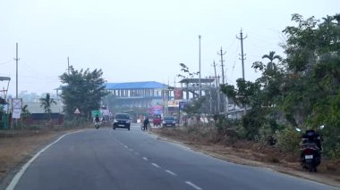 Dibrugarh, Assam, Hindistan, 15 Ocak 2026: Araçlar ve insanlar, Hindistan 'ın kuzeydoğusundaki günlük ulaşım ve yerel yaşamı gösteren, kamu binaları ve yol kenarı altyapısı yakınlarındaki yarı kentsel bir yol boyunca hareket ediyorlar.