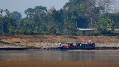 Nehir kenarında küçük bir tekne olan sakin bir nehrin geniş bir manzarası var. Uzak, tanımlanamayan insanları taşıyor. Sahne, su yüzeyindeki yansımaları, set yapılarını ve arka plandaki yemyeşil alanları gösteriyor. Doğa, yaşam tarzı ve seyahat için uygun..