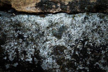 Katmanlı kaya yüzeyleri, koyu grunge lekeleri ve doğal hava koşulları içeren eski bir taş duvarın yakın çekimi. Kaba mineral dokusu ve yatay taş kenarı tasarım ve inşaat için uygun güçlü bir mimari zemin oluşturur..