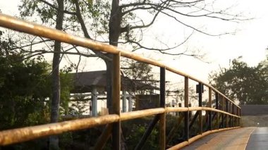 Yaya köprüsünün, ahşap korkulukları ve sıcak doğal ışıkta yakalanan metal yapısıyla yakın açılı görüntüsü. Açık hava düzeni ve öncü hatlar seyahat, yolculuk ve altyapı kavramları için uygun sakin ve minimal bir sahne oluşturur..