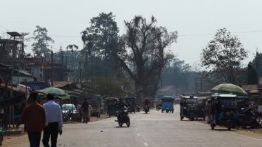 Dibrugarh, Assam, Hindistan, 12 Şubat 2026: Otomobil arabaları, motosikletler ve yayalar ile günlük trafik yolu paylaşıyor. Yol kenarındaki küçük dükkanlar, yerel işletmeler ve caddelerde sıra olan ağaçlar..