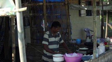 Dibrugarh, Assam, Hindistan, 17 Şubat 2026: Yerel bir sokak yemeği satıcısı, gaz sobası ve temel mutfak gereçleri kullanarak küçük bir tezgahta geleneksel yassı ekmek hazırlıyor. Adam bambu yapısı bir düzenin içinde çalışıyor, günlük hayatı yansıtıyor..