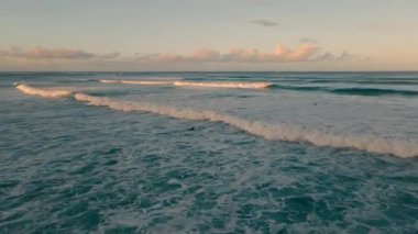 Güneş gökyüzünde batarken dalgalar kıyıya çarpıyor. Okyanus suyu, gecenin renklerini yansıtarak kıyıda doğal bir görüntü oluşturur..