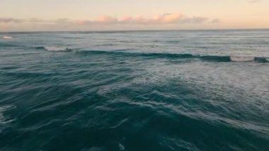 Sörfçüler Hawaii 'de günbatımında okyanus dalgalarının tadını çıkarırlar. Güneş batarken gökyüzü renkleri gösteriyor. Birçok sörfçü sudaki harika koşullardan yararlanıyor..