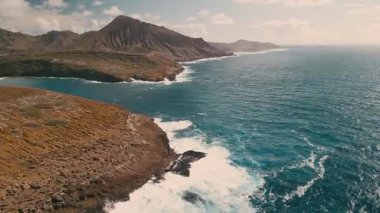 Dalgalar kıyıya çarparken kayalık kıyı şeridi boyunca yürüyüş yapmak. Okyanusun üzerindeki tepeler doğanın ve mavi suyun çarpıcı manzarasını yaratıyor..
