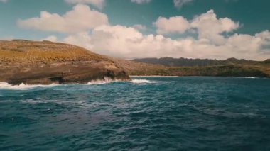 Dalgalar kayaların üzerinde yuvarlanırken güneş okyanusun üzerinde parlıyor. Manzaralı uçurumlar ve dağlar Hawaii 'deki kıyı şeridini çevreledi. Bu doğanın canlı bir sahnesi..