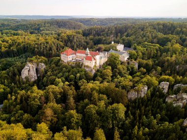 Yoğun Karışık Orman, Kızıl Döşemeli Çatı ve Taş Kuleler ile çevrelenmiş Çek Hava Görüntüsü Kalesi Rocky Outcrops 'dan Yükseliyor, Yumuşak Sabah Işığı, Gözlerden uzak Ruh hali, Miras