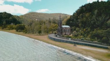 Kıyı Şapeli, Orman Kıyısı Kıyısı Dalgaları, Taştan Kilisenin İHA 'sını Uzun Spire, Sarmal Sahil Yolu, Kumsal Sahili ve Sakin Turkuaz Suyu ile çevrili