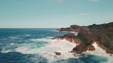 Çakılan Dalgalar, Siyah Volkanik Uçurumlar ve Turkuaz Atlantik Suyu ile Hava Asmaları Kıyısı. İnsansız hava aracı engebeli bazalt sahillerinde sörf yaparken Kaya koylarında köpük bulutsuz gökyüzüne sıçrıyor..