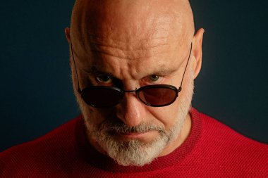 Yakından Kel Adam, Güneş Gözlüğü, Kırmızı Kazak, Gergin Bakış, Stüdyo Işıklandırma, LowKey Moody Atmosfer, Deneyimli Danışman Persona, Buruşuk Alnlı, Tuzlu Sakal, Vintage
