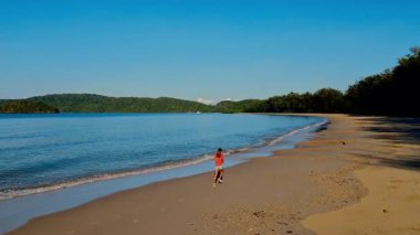 Sabahları kumsalda koşan çocuk Dalgalar ve uzaktaki ağaçlarla, tasasız hareketlerle