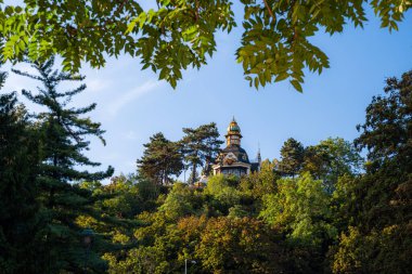 Tepe üzerindeki tarihi şato. Etrafı gür ağaç tepe örtüsüyle çevrili. Süslü kuleler, sıcak güneş ışığı, berrak mavi gökyüzü.,