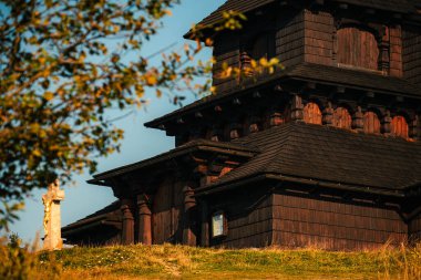 Çerçevelenmiş tepedeki ahşap kilise. Çimentolu yamaçta tünemiş ağaç, çok katmanlı çatı ve uzun Spire.,