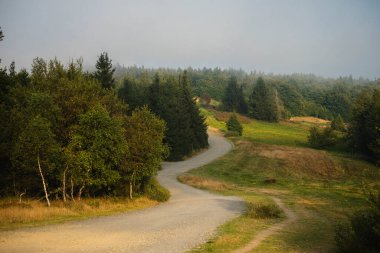 Kavisli çakıllı yol, tepelerden geçip, yumuşak kıvrımlı, güneşli çayırlara doğru gidiyor.